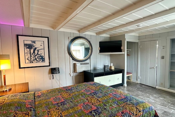 A hotel room with a bed, a desk, a TV, a mirror, and a wardrobe.