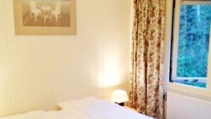 Hotellihuone, jossa on sänky, lamppu, ikkuna, jossa on verhot, ja seinällä oleva kehystetty kuva.