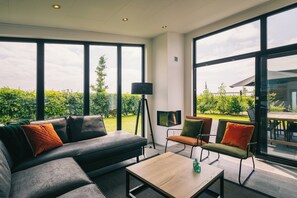 Ein modernes Wohnzimmer mit Sofa, Sesseln, Couchtisch und großen Fenstern mit Blick auf Grünflächen.
