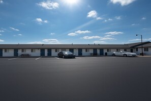 A motel with a parking lot, two cars, and a clear blue sky.