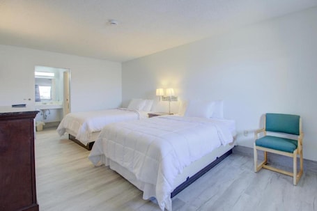 A hotel room with two beds, a wooden chair, a desk, and a mirror.. 2 Queen Beds|Non-Smoking