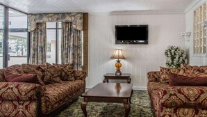 Quarto com sofás estampados, uma mesa de centro de madeira, uma televisão e uma janela com cortinas.