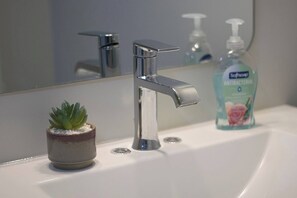 A bathroom sink with a chrome faucet, a small potted plant, and a bottle of antibacterial soap.