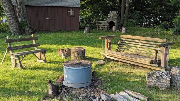 A rustic outdoor setting with a fire pit, benches, and a small shed.
