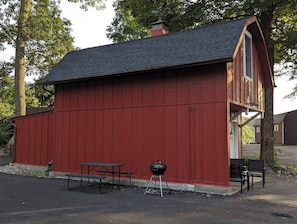 Un edificio in legno rosso con un portico coperto, un tavolo da picnic e un barbecue.