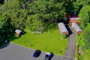 Eine Vogelperspektive auf einen Parkplatz mit zwei Autos, umgeben von Grünflächen und Bäumen, mit Gebäuden im Hintergrund.