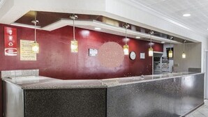Uma área de recepção com balcão de mármore, luminárias pendentes e um relógio na parede.