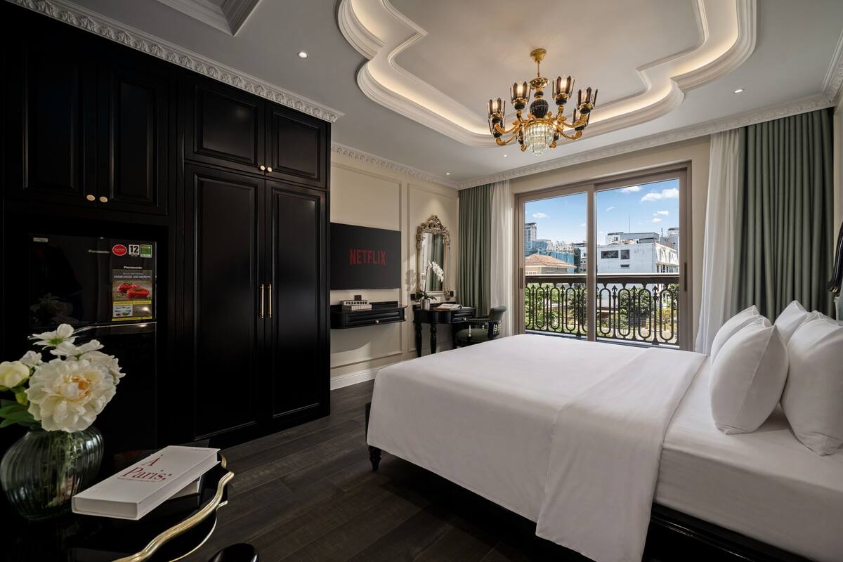Quarto de hotel com uma cama grande, minibar, televisão, vista da cidade e varanda com guarda-corpo.