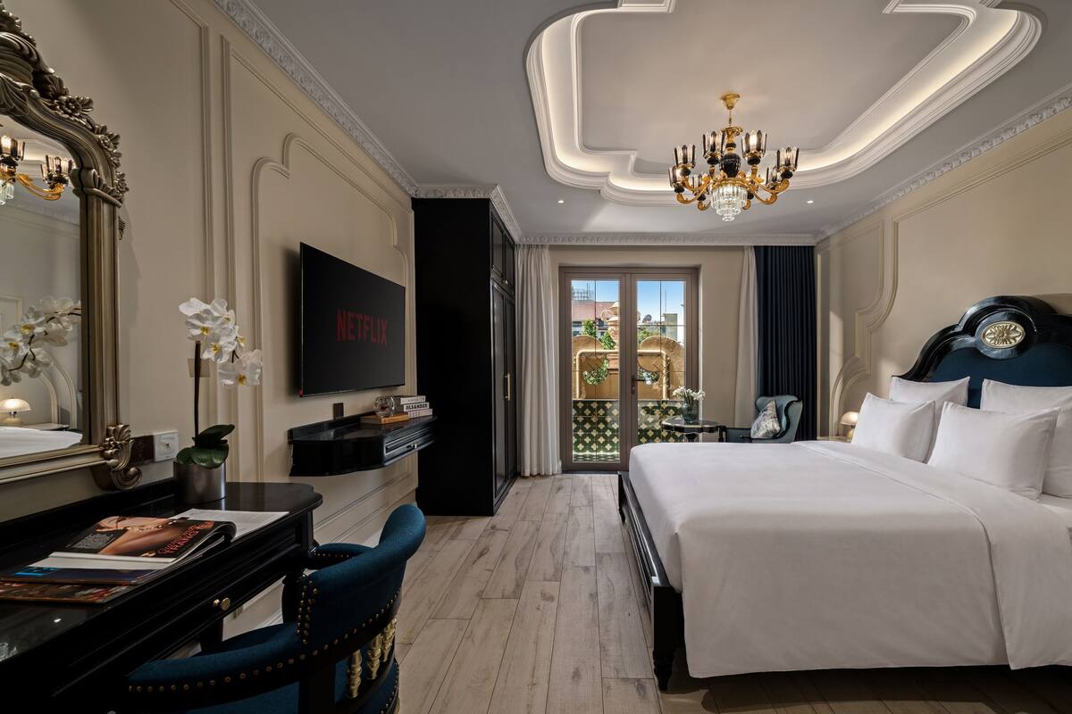Quarto de hotel com uma cama grande, televisão, escrivaninha com cadeira e vista para o exterior.
