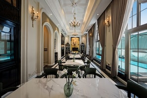 Une salle à manger formelle avec des tables en marbre, des chaises élégantes, des lustres et de grandes fenêtres.