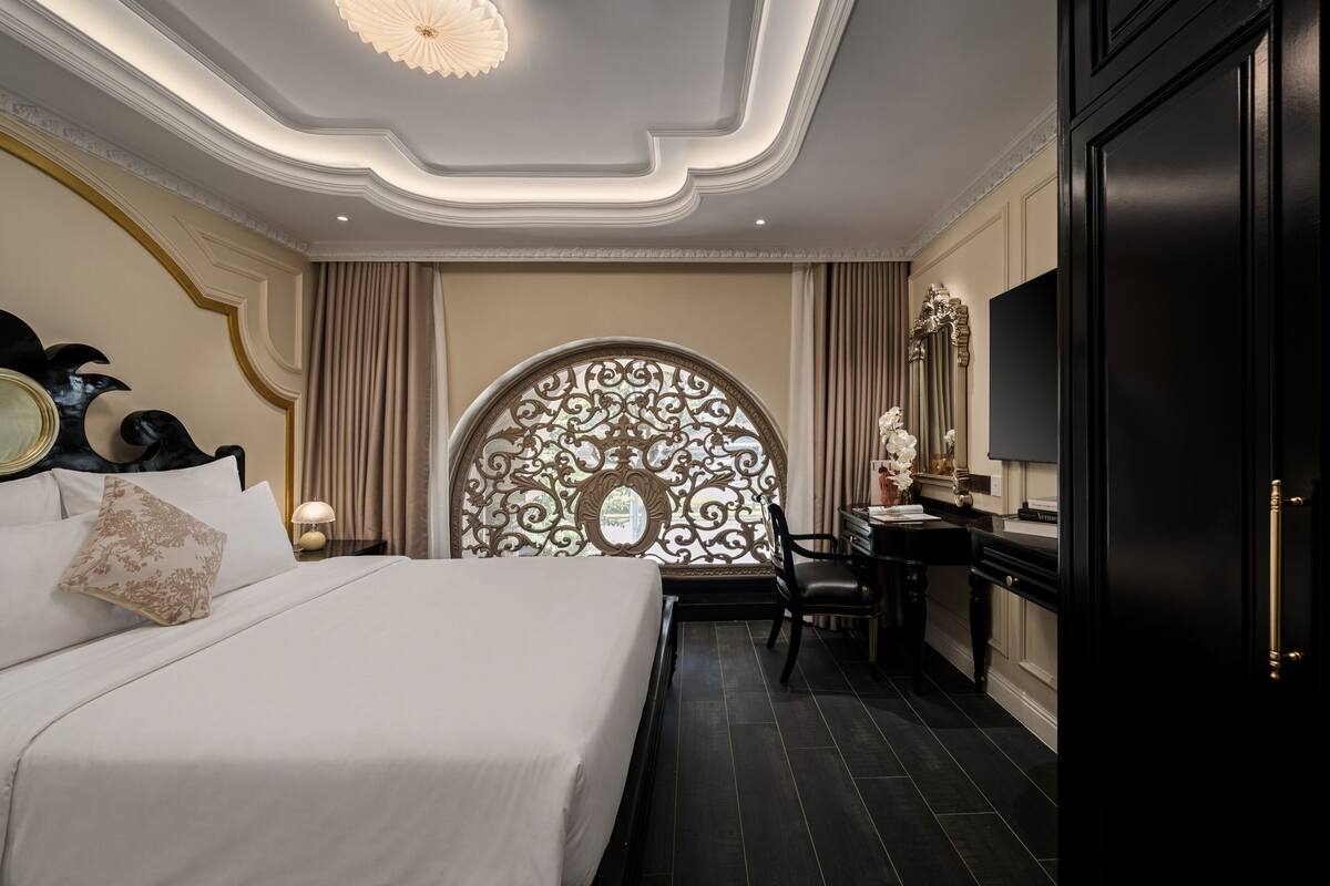 Quarto de hotel com uma cama grande, uma escrivaninha, uma cadeira, uma toucador com espelho e um painel decorativo na parede.