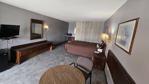 Una camera d'albergo con un letto, una scrivania, una sedia, una televisione, una lampada e un quadro appeso al muro.