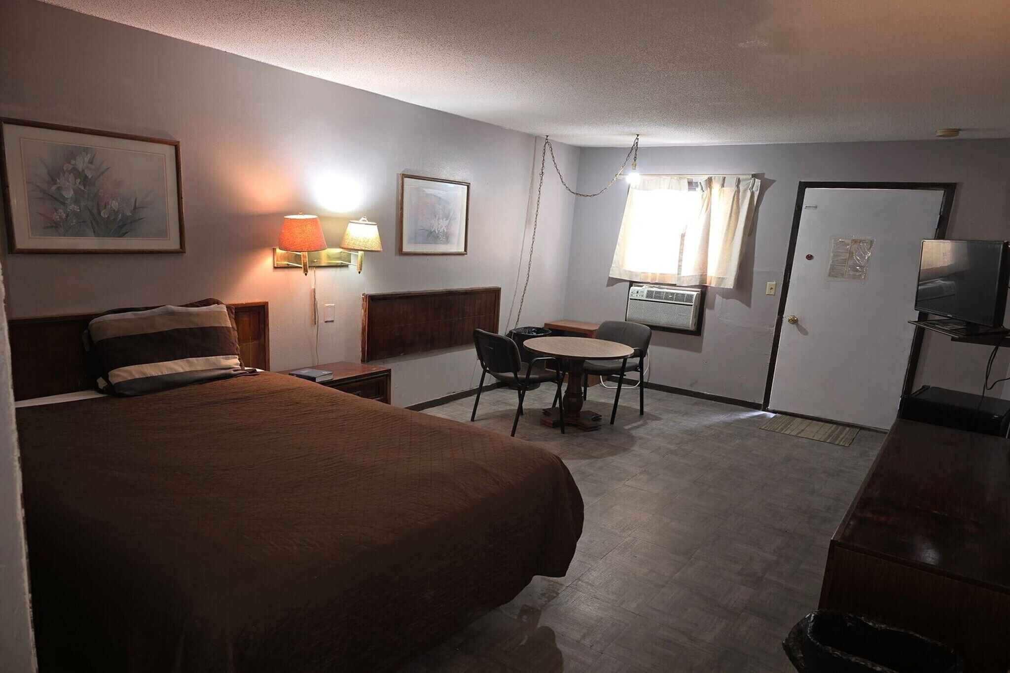 A hotel room with a bed, a desk, a chair, a lamp, and a television.