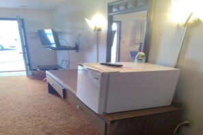 Una habitación con escritorio, silla, refrigerador pequeño, televisor montado en la pared y espejo.