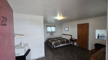 Ein Schlafzimmer mit Bett, Schreibtisch, Mikrowelle, einer Tür und einem Fenster mit Vorhängen.