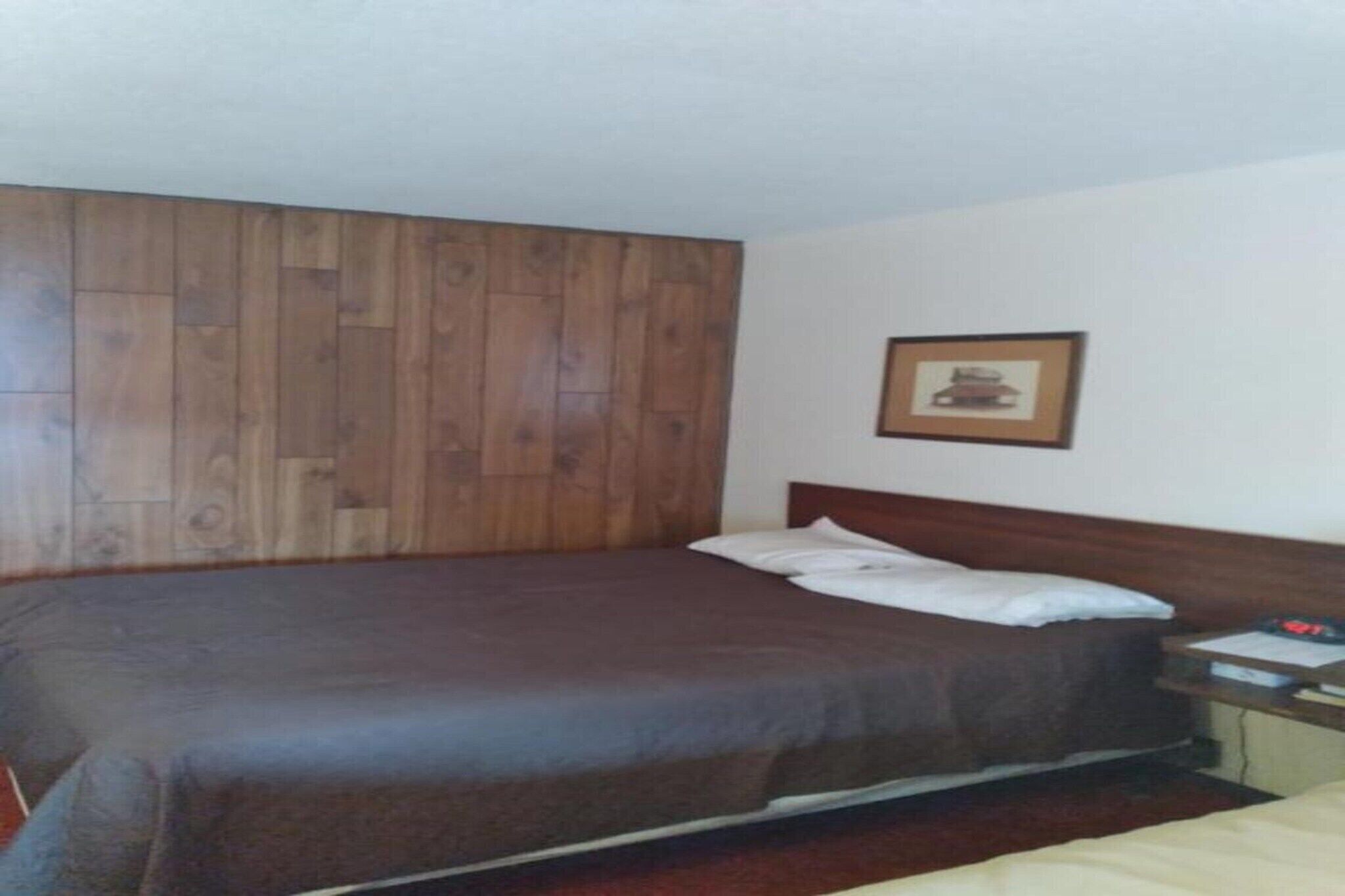 A single bed with a wooden headboard, a bedside table with a lamp, and a framed picture on the wall.