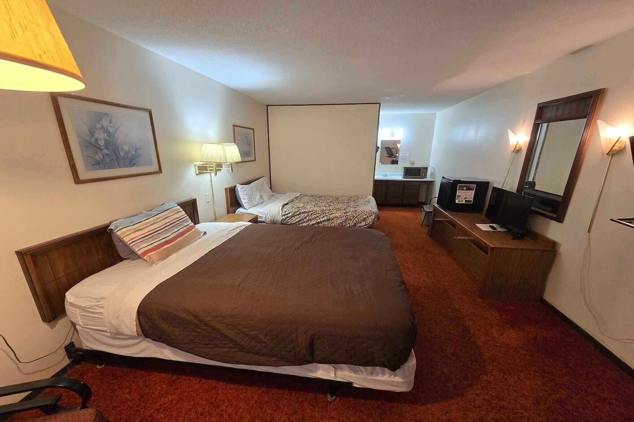 A hotel room with two beds, a desk, a chair, a TV, and a mirror.