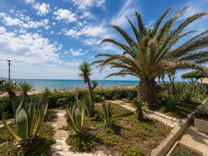 A coastal garden with palm trees, agave plants, and a pathway leading to the beach. - La Casa in Riva al Mare by Geco Vacation Rentals (Caucana)