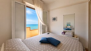 A bedroom with a bed, a bedside table, a mirror, and a view of the sea. - La Casa in Riva al Mare by Geco Vacation Rentals (Caucana)