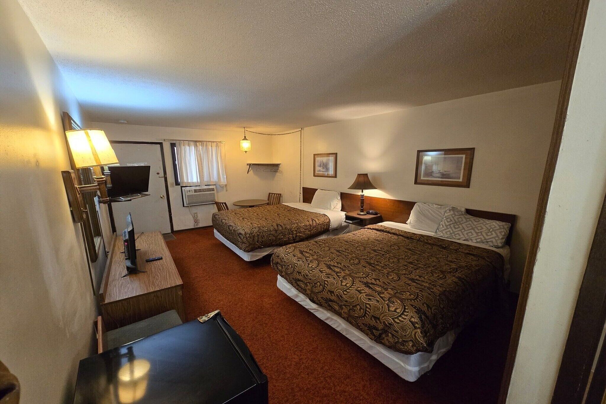 A hotel room with two beds, a desk, a television, and a window with curtains.