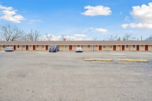 Un motel con una fila de habitaciones, un estacionamiento y cielo despejado.