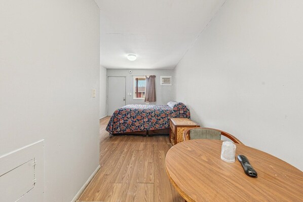 A small, narrow room with a bed, a table, and a chair.