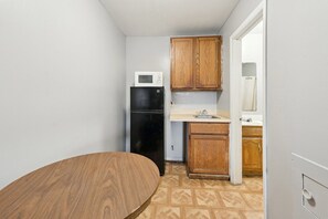 A compact kitchen with a microwave, refrigerator, wooden cabinets, and a sink. - Queen Bed|Smoking|Flint MI (Flint MI)