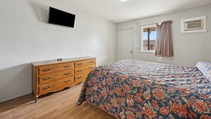 Een slaapkamer met een bed, een dressoir, een televisie aan de muur en een raam met gordijnen.