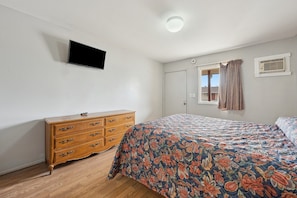 A bedroom with a bed, a dresser, a television on the wall, and a window with curtains. - Queen Bed|Smoking|Flint MI (Flint MI)
