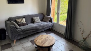 A grey sofa with patterned cushions, a round wooden table, and a painting of waves on the wall. - Chalet between land and sea (Ambrumesnil)