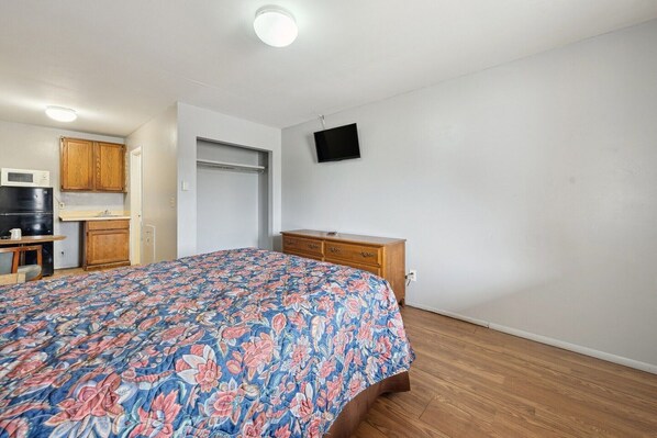 A bedroom with a floral bedspread, wooden dresser, and a television on the wall.