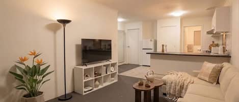 Uma sala de estar com televisão, sofá, mesa de centro, abajur e um vaso com planta.