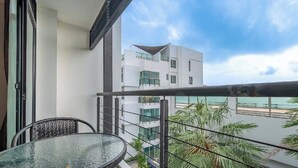 Un balcon avec une table et des chaises en verre, donnant sur un immeuble moderne et une plage.