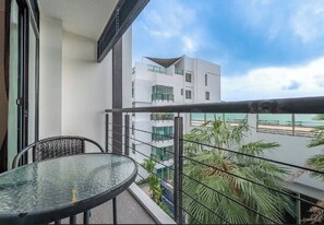 Ein Balkon mit Glastisch und Stühlen, der einen modernen Gebäudebereich und einen Strand überblickt.