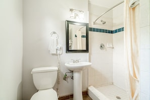 A bathroom with a toilet, sink, mirror, and shower.