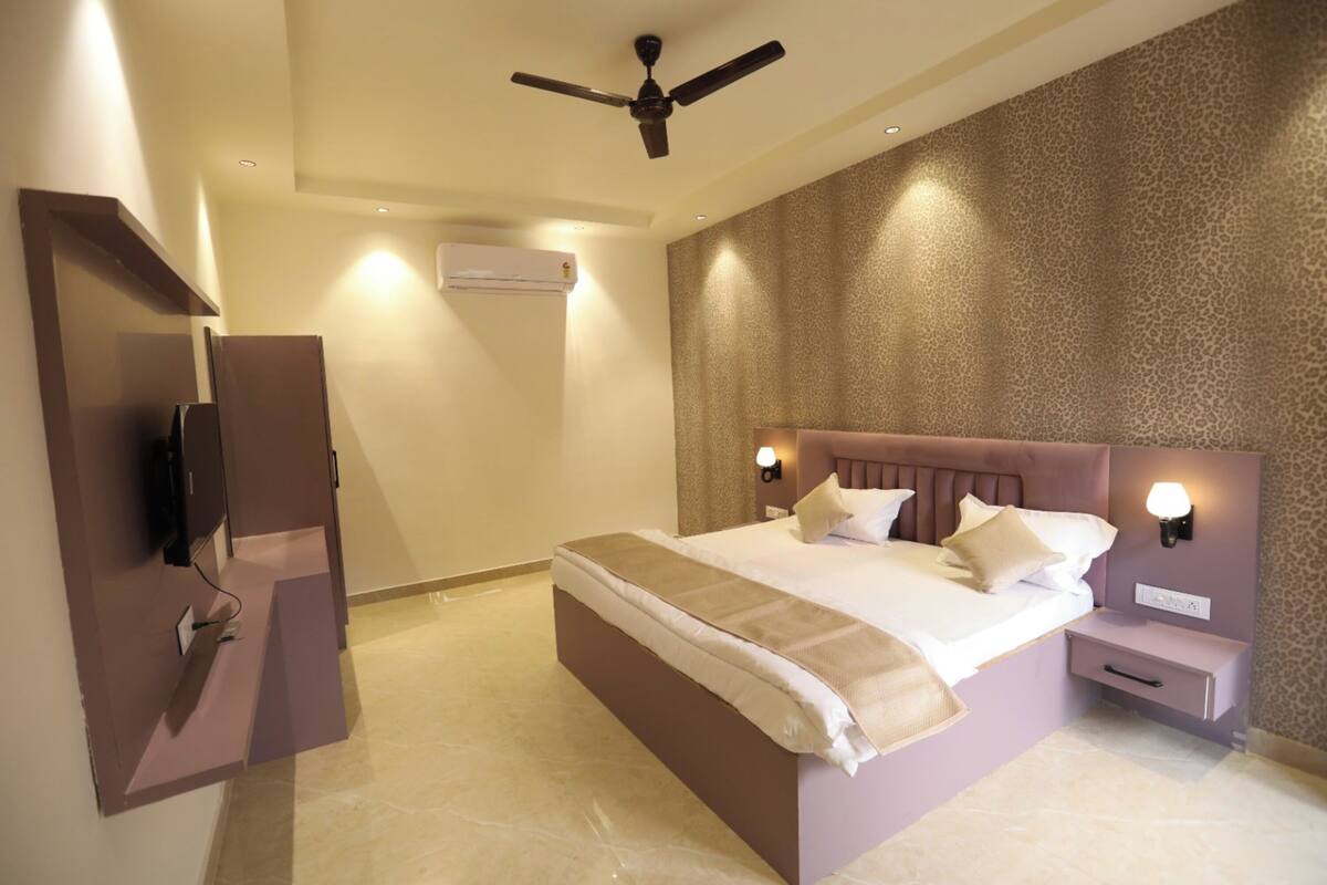 Un dormitorio con cama, mesitas de noche, ventilador de techo, equipo de aire acondicionado y televisor instalado en la pared.