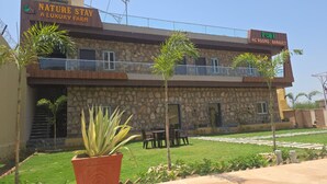 Un edificio de dos pisos con fachada de piedra, un balcón y un letrero que dice 'Nature Stay Luxury Farm' y 'Habitaciones con aire acondicionado y salón de banquetes'.