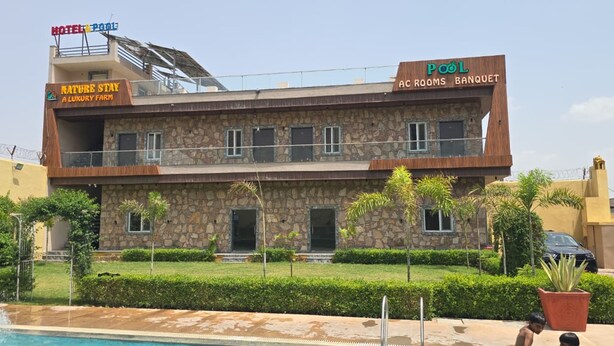 Edificio de dos pisos con fachada de piedra, piscina en primer plano y señalización que indica 'Nature Stay Luxury Farm' y 'Habitaciones con aire acondicionado junto a la piscina y salón de banquetes'.