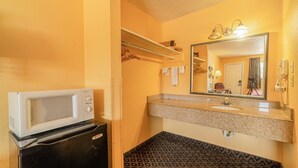Un baño de hotel pequeño con microondas, lavabo, espejo y suelo estampado.