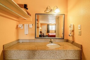 A bathroom with a granite countertop, a sink, a mirror, a towel rack, and a hairdryer. - 2 Queen Bed|Smk|Falfurrias TX (Falfurrias TX)