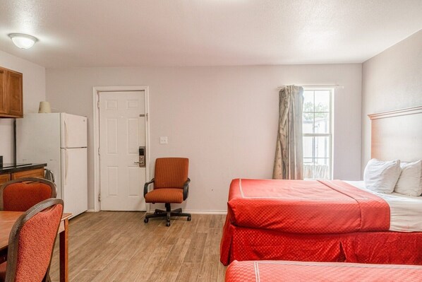 A compact room with a bed, a chair, a desk with a refrigerator, and a window with curtains.