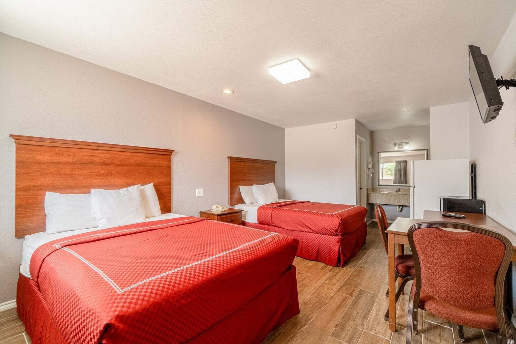 Habitación de hotel con dos camas, un escritorio, una silla, un televisor y un baño visible al fondo.