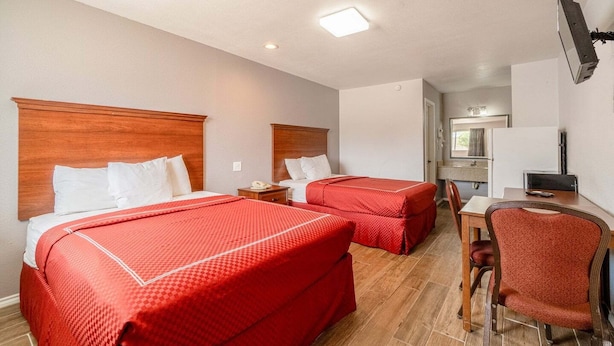 A hotel room with two beds, a desk, a chair, a TV, and a bathroom visible in the background. - 2 Queen Bed|Smk|Falfurrias TX (Falfurrias TX)