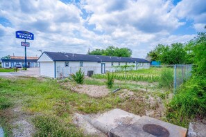 A Budget Inn motel with a fenced parking area and a grassy field. - 2 Queen Bed|Smk|Falfurrias TX (Falfurrias TX)