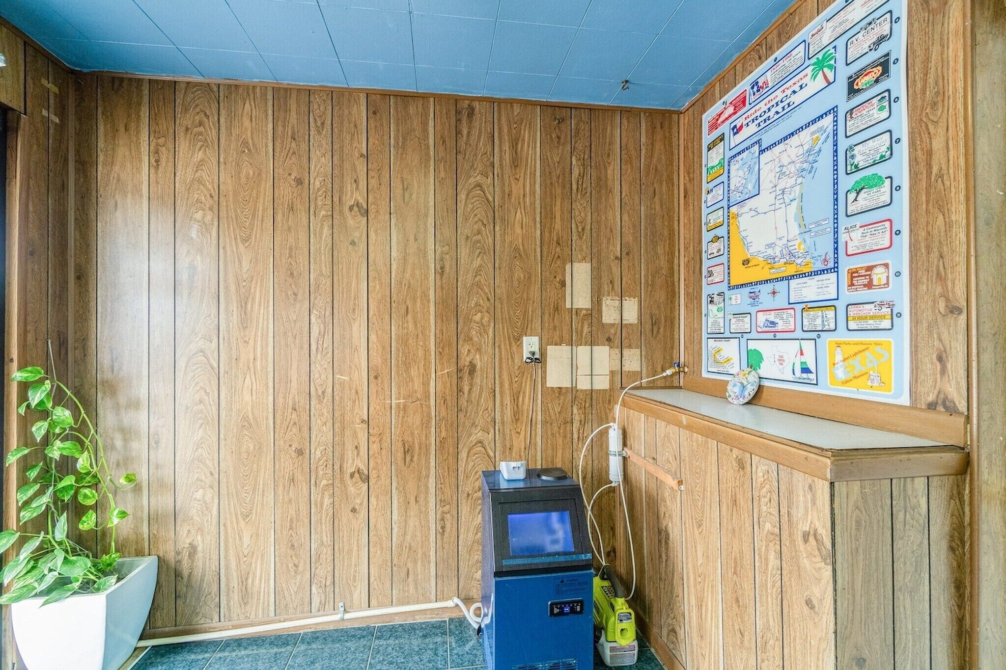 A room with wooden panel walls, a map on the wall, a small desk, and a plant.
