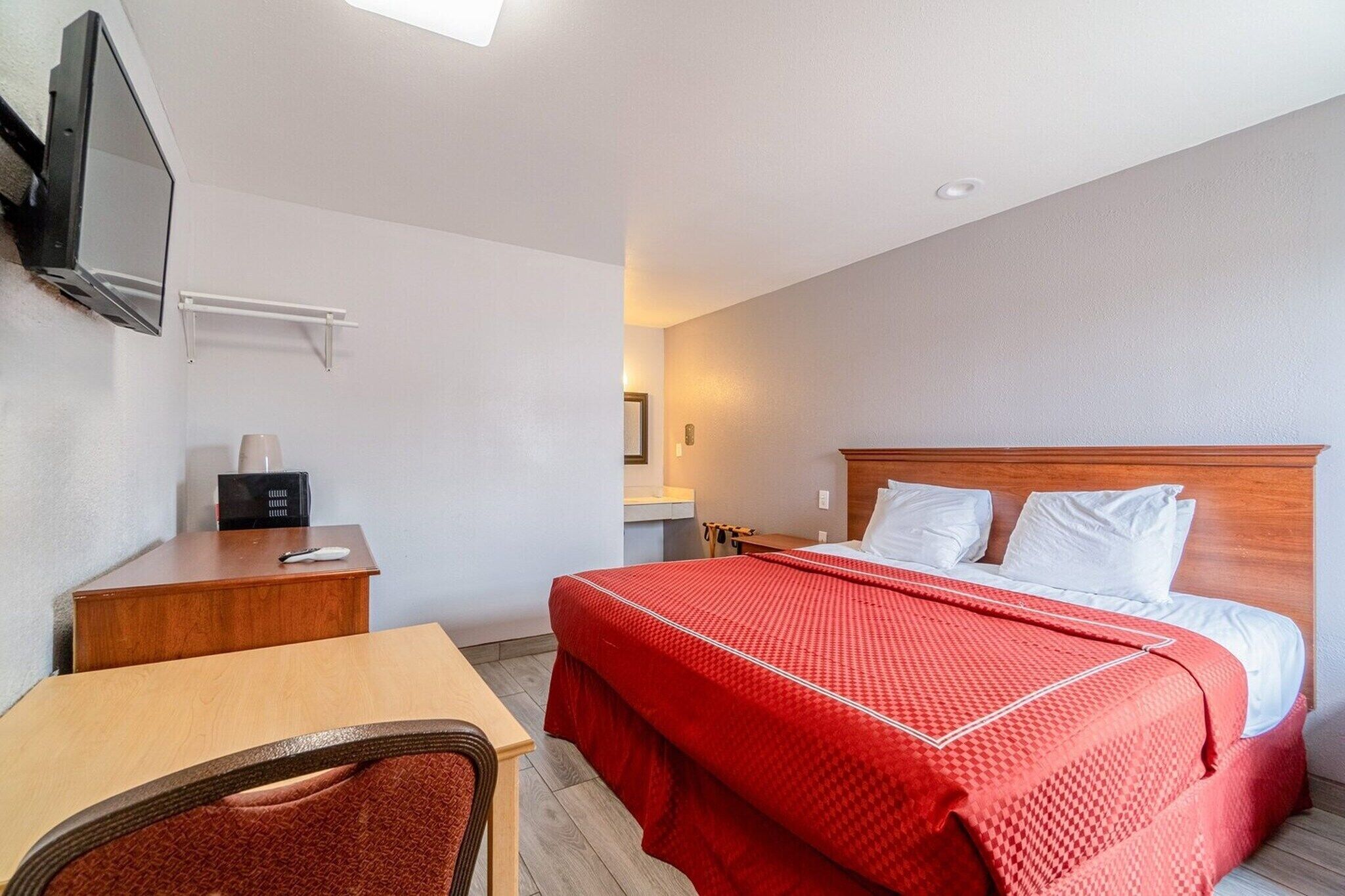 Habitación de hotel con cama, escritorio, silla, televisor montado en la pared y mesita de noche.