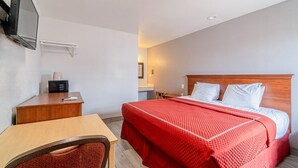 Ein Hotelzimmer mit einem Bett, einem Schreibtisch, einem Sessel, einem an der Wand befestigten Fernseher und einem Nachttisch.