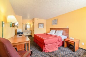 A hotel room with a bed, desk, chair, lamp, and a mirror.