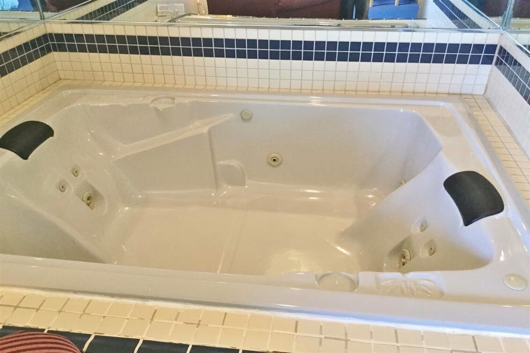 Un bain à remous rectangulaire, doté d’un bord carrelé, d’un drain et de deux repose-pieds noirs.