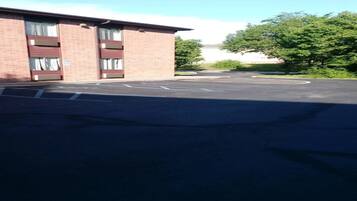 A parking lot with a building that has multiple garage doors, a clear sky, and trees in the background.